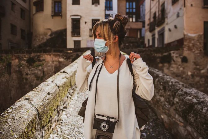 Туристка в маске и с фотоаппаратом гуляет по историческим руинам